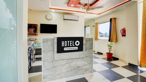 A hotel reception area with a marble counter, a clock, an air conditioning unit, a television, a ceiling fan, and a window with curtains. - Classic Hotel Shimla Grand (Lucknow)