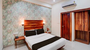 A bedroom with a bed, wooden headboard, floral wallpaper, a nightstand, an air conditioning unit, and a wardrobe. - Classic Hotel Shimla Grand (Lucknow)