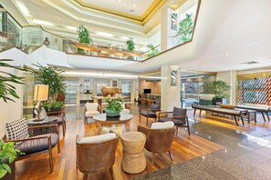 A spacious lobby with a high ceiling, multiple seating areas, and a central plant arrangement. - Luana at Waikiki 1-Bed Ocean View Getaway in the Heart of Waikiki (Honolulu)