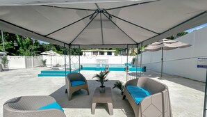 Ein Sitzbereich im Freien mit Pool, beschattet durch einen großen Sonnenschirm, umgeben von weißen Wänden.