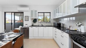 A modern kitchen with white cabinets, a black countertop, stainless steel appliances, and a dining area with a table set for four. - 4BR Carlisle Stay Near Airport & Stadium  Sleeps 8 (Carlisle)