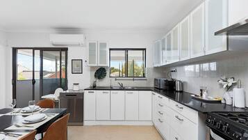 A modern kitchen with white cabinets, a black countertop, stainless steel appliances, and a dining area with a table set for four.