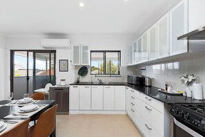 Een moderne keuken met witte kasten, een zwart aanrecht, roestvrijstalen apparatuur en een eethoek met een tafel voor vier personen.