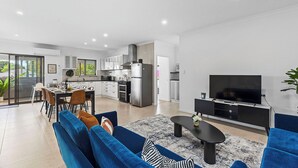 A modern living room with a sofa, coffee table, and TV. Adjacent is a kitchen with white cabinets and a dining area with a table set for four. - 4BR Carlisle Stay Near Airport & Stadium  Sleeps 8 (Carlisle)