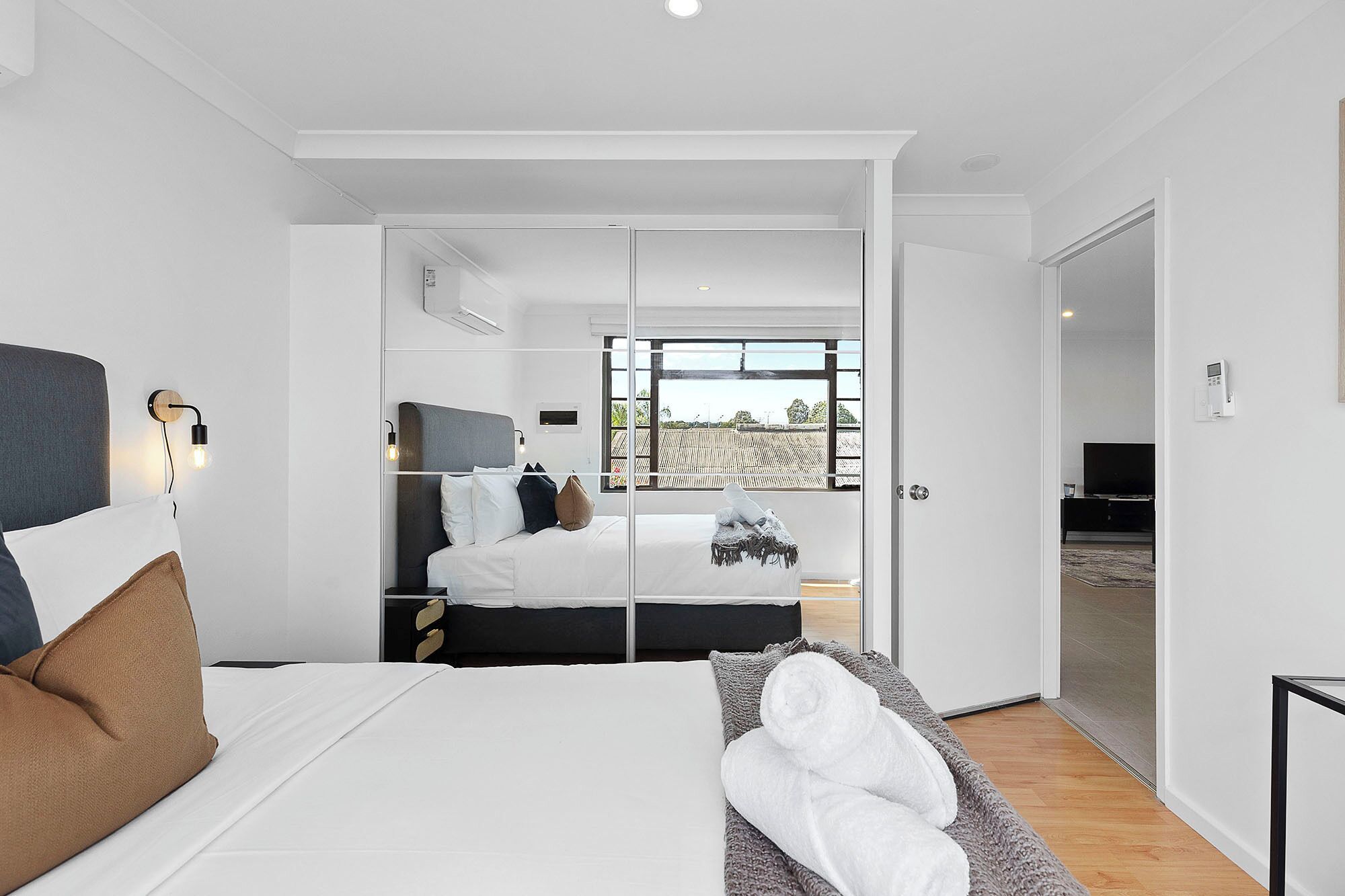 A modern bedroom with a bed, bedside tables, a wardrobe, and a large window.