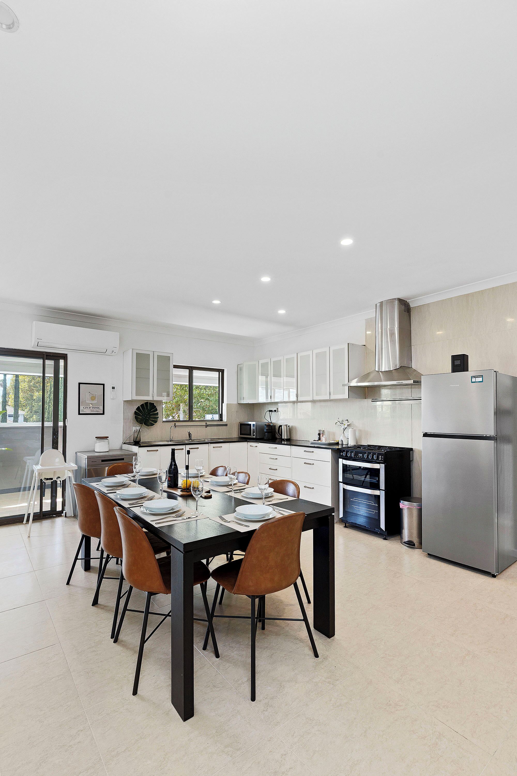 A modern kitchen with a dining area, stainless steel appliances, and a large window.