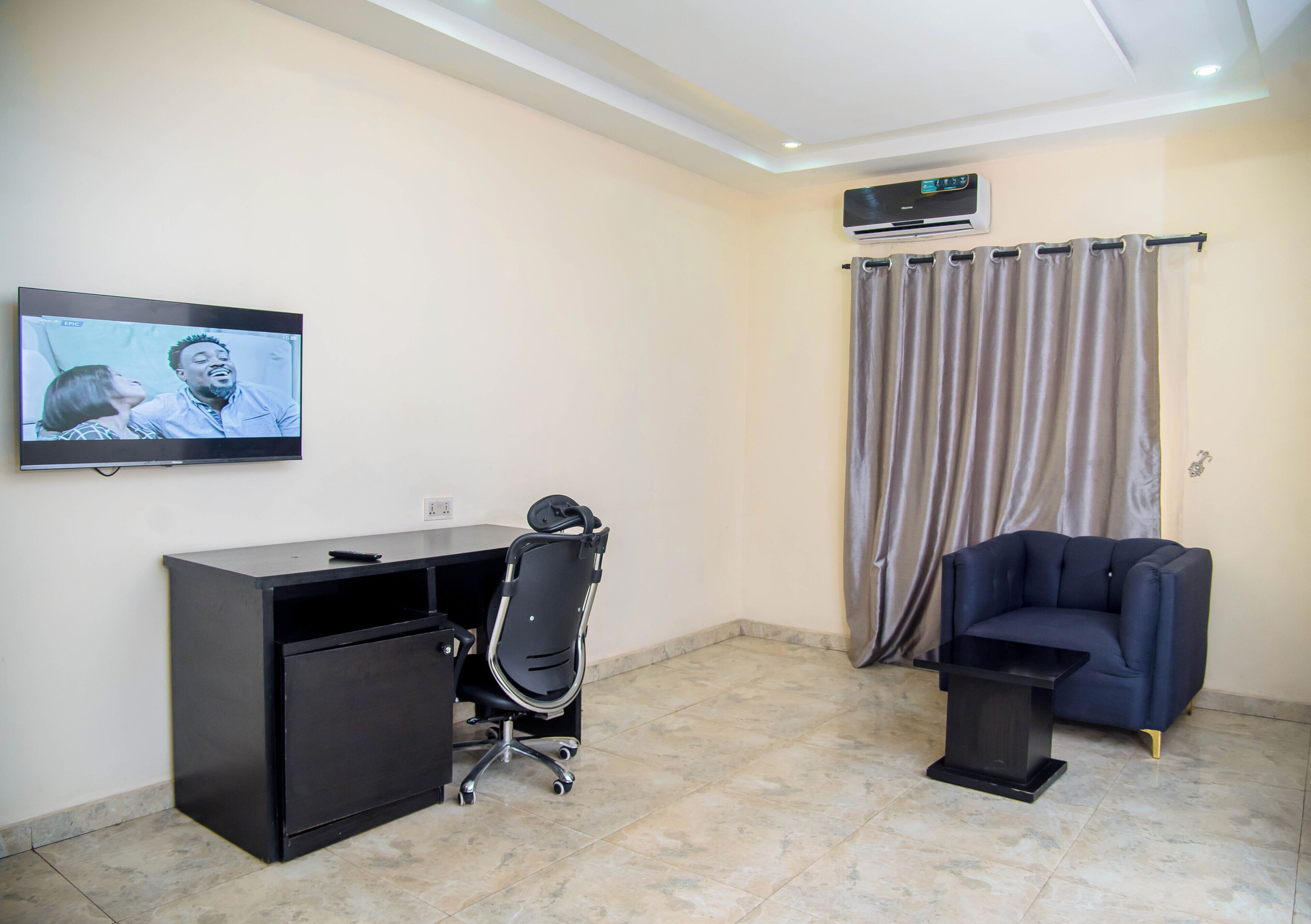 Une pièce comprenant un bureau, une chaise, un téléviseur, un climatiseur et un canapé.