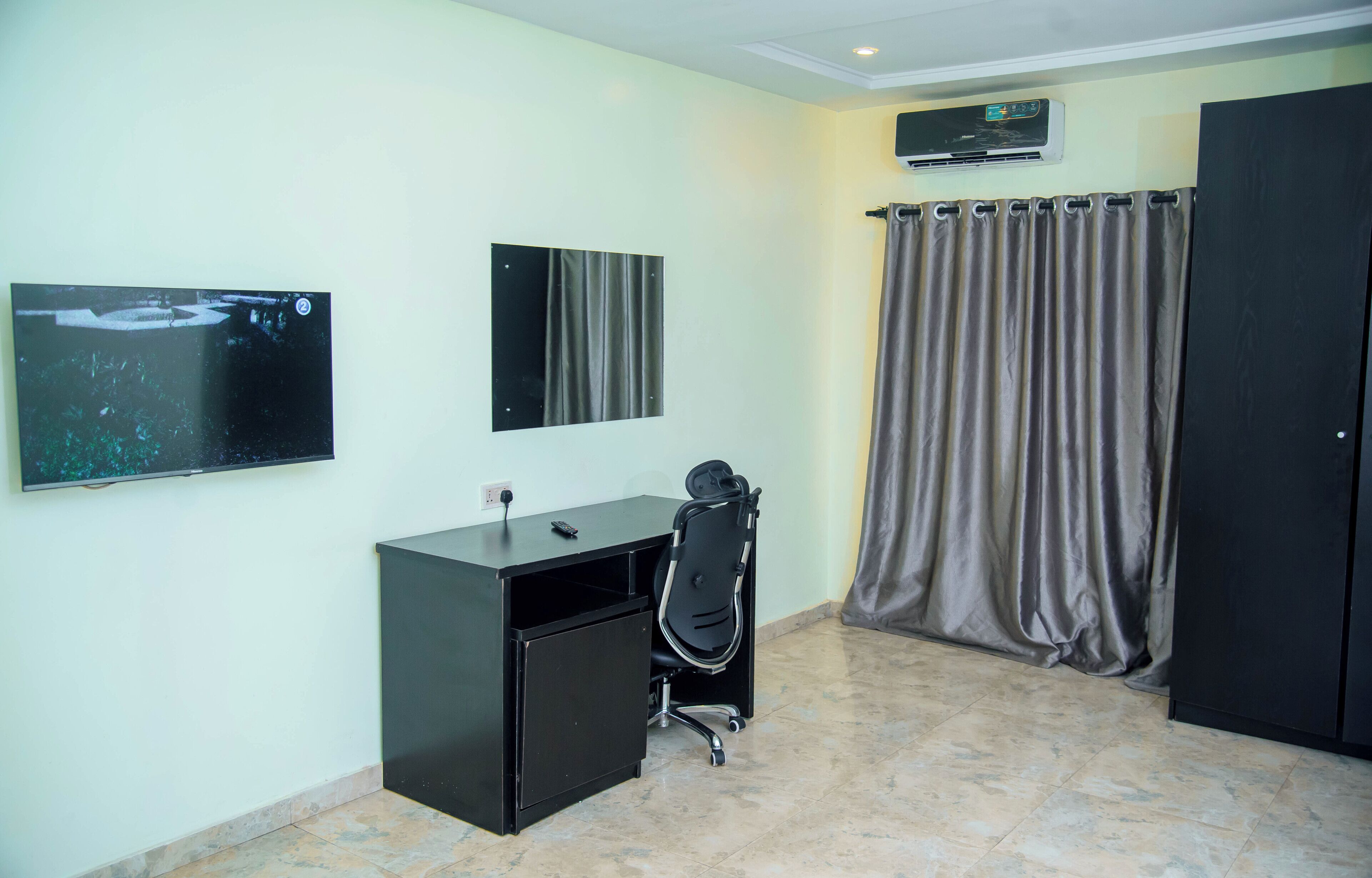 A room with a desk, chair, two wall-mounted TVs, a curtain, and a door.