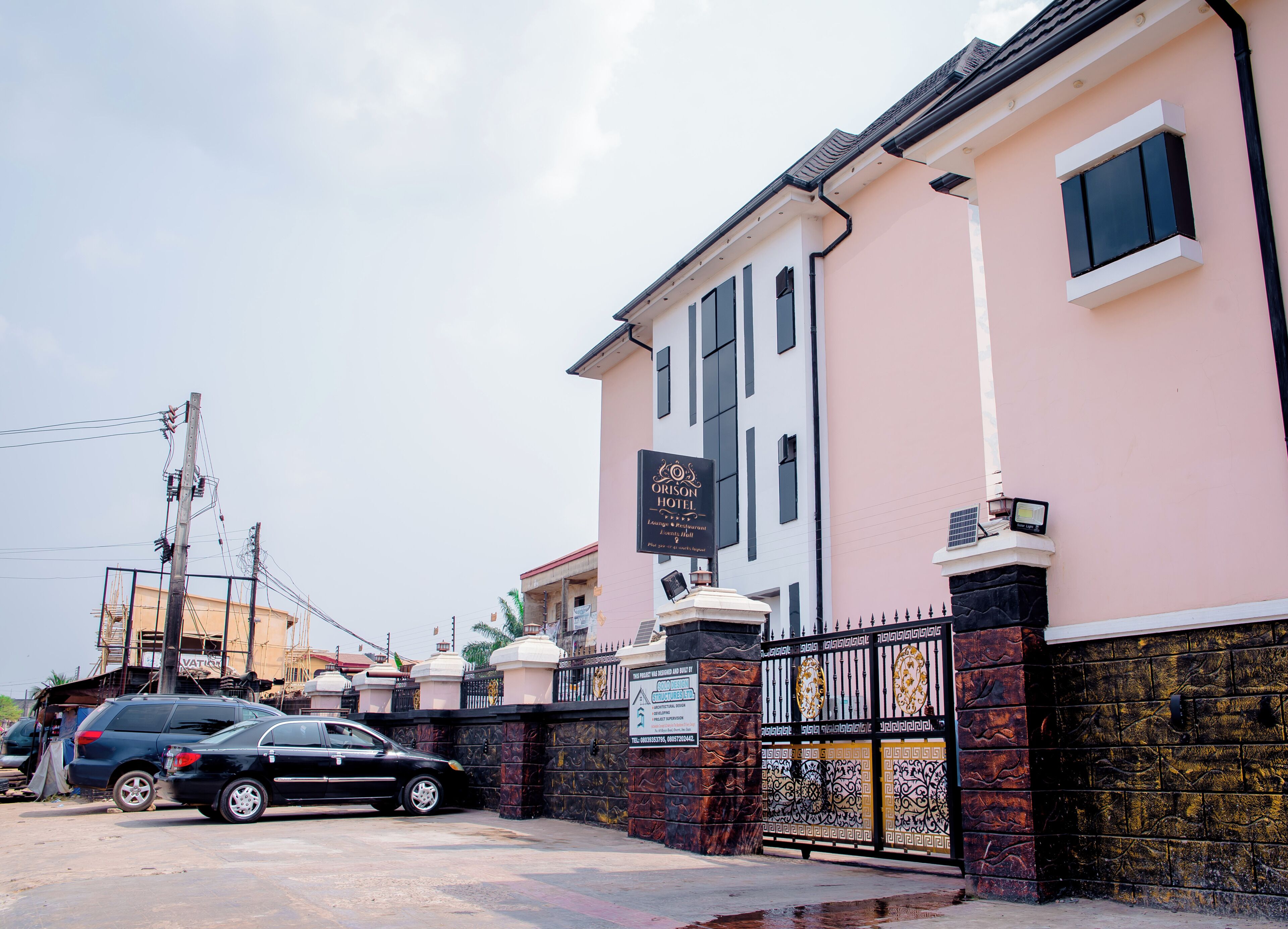 A hotel with a signboard, a gated entrance, and a parked car.