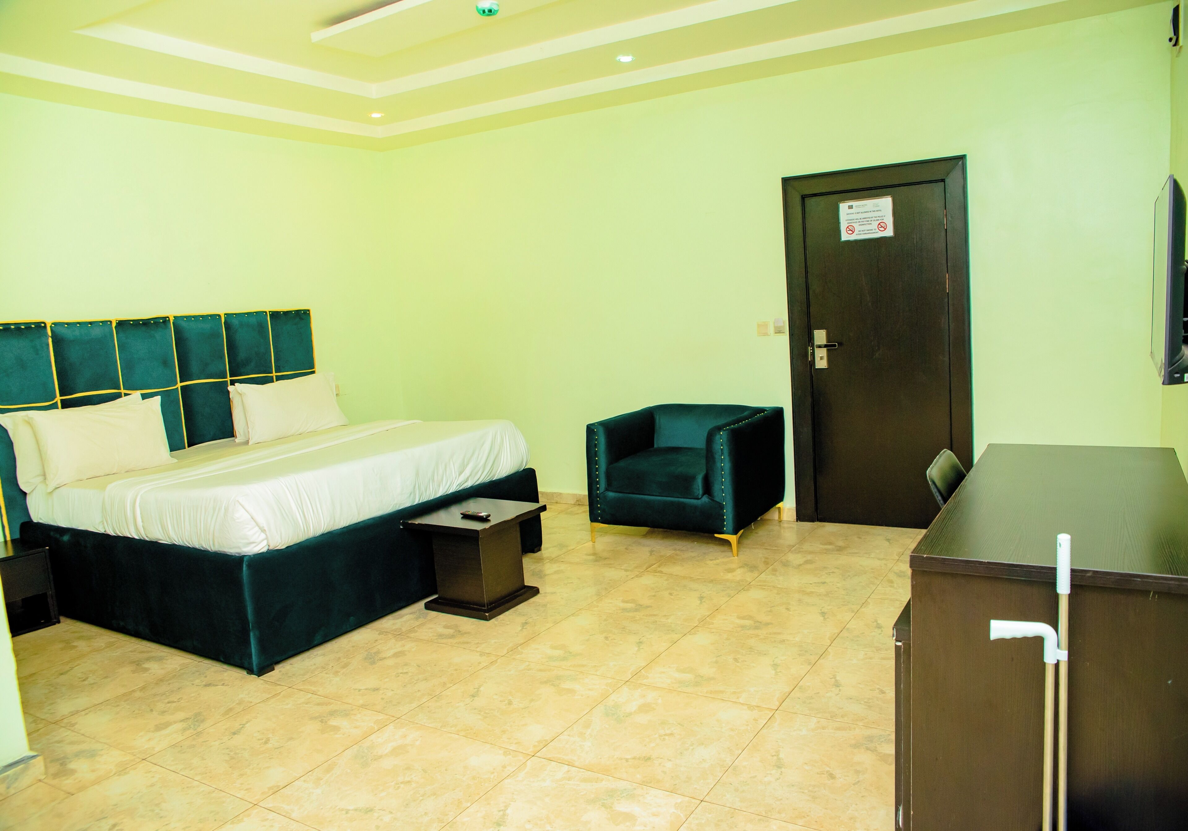 A hotel room with a bed, a small table, a chair, a desk, and a door.