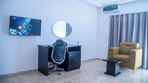 A modern room with a desk, chair, TV, air conditioning unit, and a window with curtains. - Orison Hotel (Owerri)