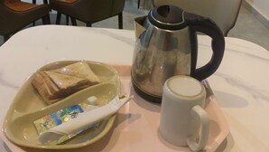 A breakfast tray with toast, a mug, and a coffee pot on a table in a hotel dining area with chairs and tables. - Orison Hotel (Owerri)