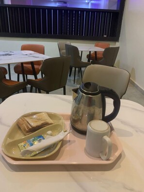 A breakfast tray with toast, a mug, and a coffee pot on a table in a hotel dining area with chairs and tables. - Orison Hotel (Owerri)