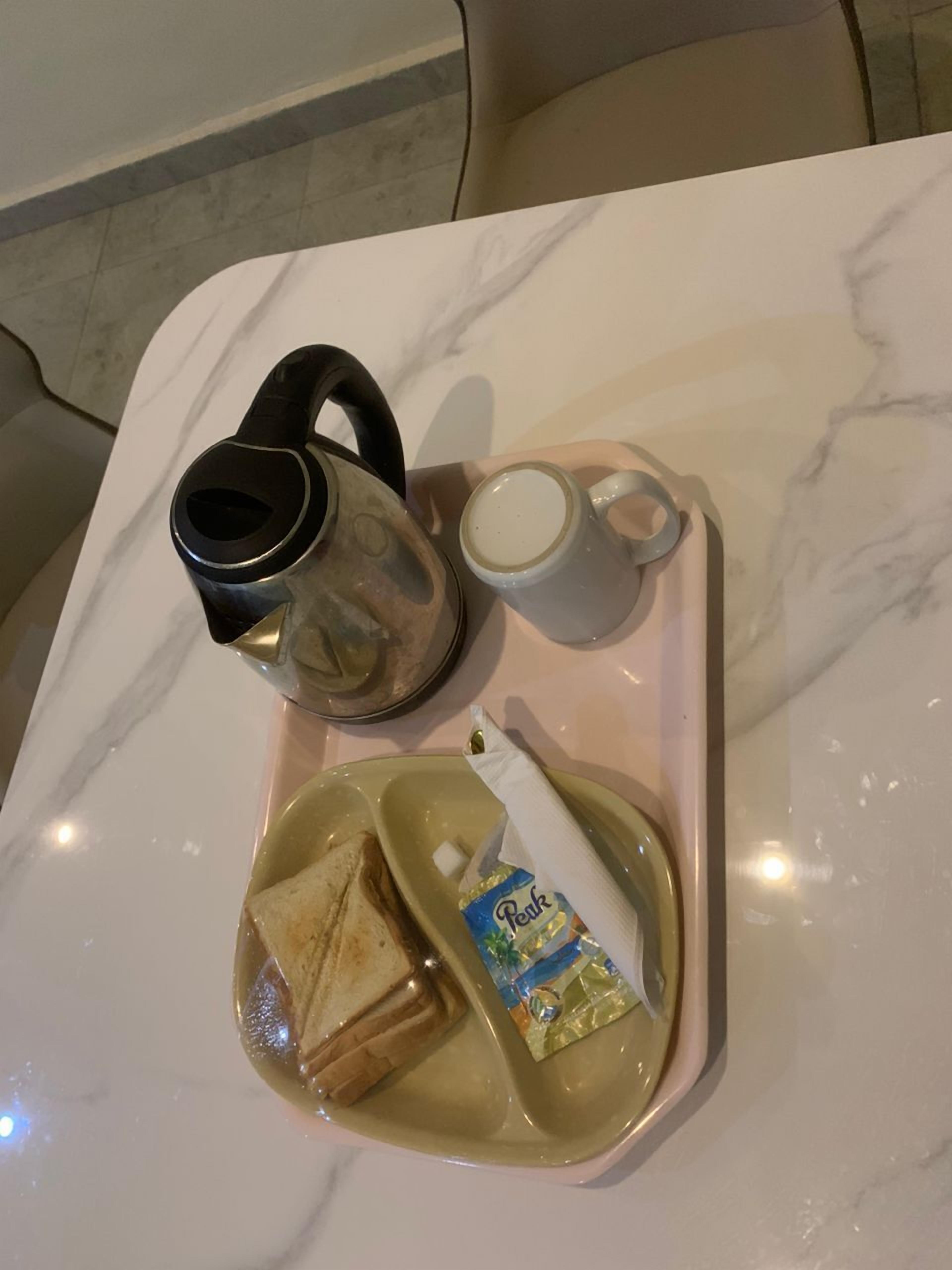 Ein Tablett mit Teekanne, Tasse, Sandwich und einem Beutel Instantkaffee auf einer Marmortafel.