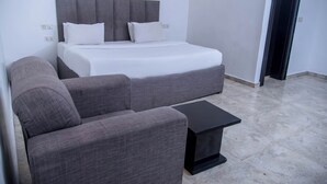 A modern hotel room with a bed, a grey sofa, and a small black side table. - Orison Hotel (Owerri)