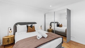 Ein modernes Hotelzimmer mit einem großen Bett, einem Holznachttisch, einem Spiegel und einem kleinen Tisch mit einer Lampe.