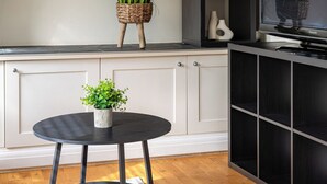 A room with a round table, a black cabinet, a white cabinet, a clock, and framed pictures on the wall. - One Bedroom Apartment in West Kensington (London)