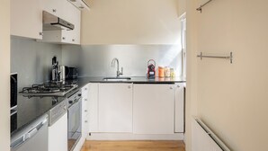 A compact kitchen with a gas stove, oven, sink, and white cabinetry. - One Bedroom Apartment in West Kensington (London)
