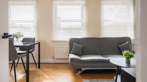 A living room with a grey sofa, a dining table with chairs, and a small table with a plant. - One Bedroom Apartment in West Kensington (London)