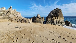 A beach with large rock formations and footprints in the sand. - Walk to Beach Modern Oceanview Villa w/ 2 Pools, Hot Tub & Concierge Cabo (Cabo San Lucas)