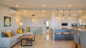 A modern kitchen with a central island, bar stools, and a dining area with a wooden table and chairs. - Walk to Beach Modern Oceanview Villa w/ 2 Pools, Hot Tub & Concierge Cabo (Cabo San Lucas)