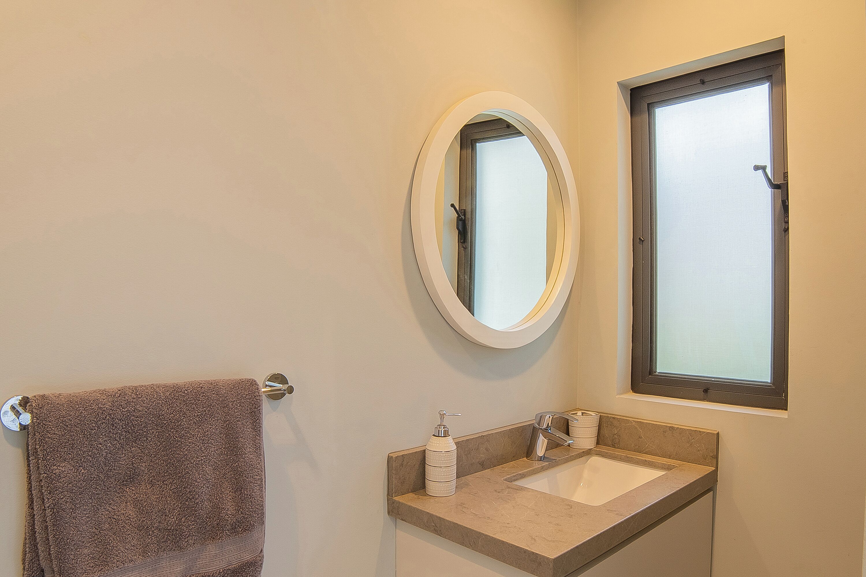 Une salle de bain avec un porte-serviettes, un lavabo avec un miroir au-dessus et une fenêtre.