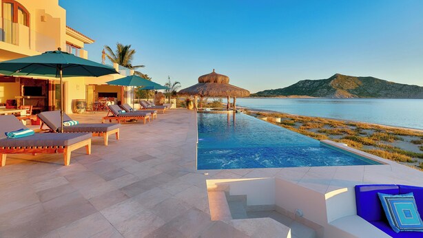 Área na piscina com espreguiçadeiras, guarda-sóis e vista para o mar.