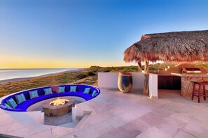 A curved blue seating area with a fire pit, a stone fireplace, and a bar area with a large vase and stools. - Beachfront Dual Villas w/ Staff&Cook, Infinity Pools, Hot Tub & Swimmable Beach (Los Frailes)