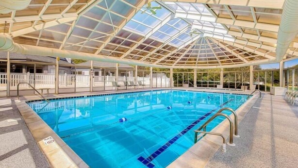 Ein Hallenbad mit Glasdach, deutlich markierten Bahnen und einem Poolbereich mit Liegestühlen.