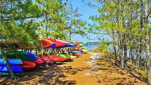 Ein Strand mit bunten Kajaks und Kanus, die unter Sonnenschirmen aufgereiht sind.