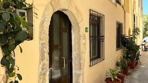 A building with a stone arch doorway, a window with metal bars, and potted plants along the sidewalk. - Casa Joanna Old Town Rethymno (Rethymno)