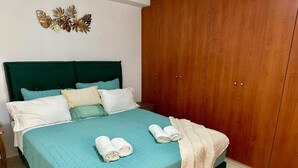 A neatly made bed with a teal bedspread, two rolled towels, and a beige throw blanket. - Casa Joanna Old Town Rethymno (Rethymno)