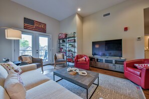 Uma sala de estar com sofá, cadeiras, mesa de centro, televisão e estante de livros.