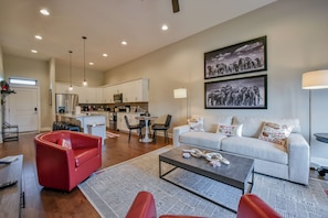 A modern living room with a red sofa, a grey sofa, and a coffee table. There is a kitchen in the background with white cabinets and a refrigerator.