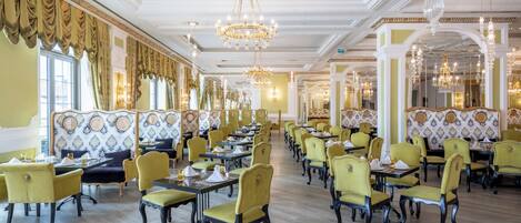 A spacious dining area with high ceilings, chandeliers, and yellow chairs.