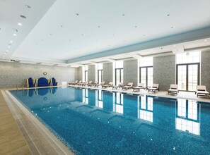 A large indoor swimming pool with lounge chairs and a stone wall.
