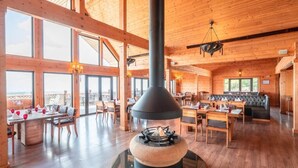 A spacious wooden interior with a central fireplace, large windows, and a dining area. - Quba Palace Hotel & Golf Resort (Quba)