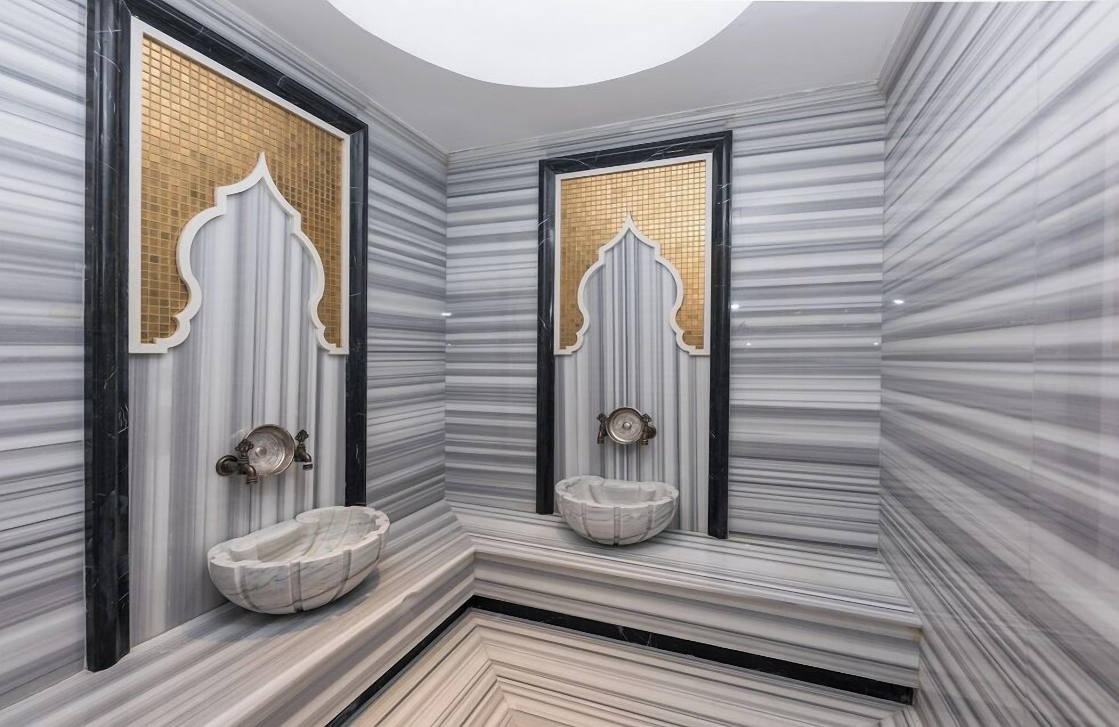 Un baño con dos lavamanos de mármol, un ventanal de mosaico dorado y suelo de mármol.
