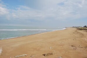 Une vaste plage de sable fin, avec des vagues douces, un ciel dégagé et une côte lointaine.