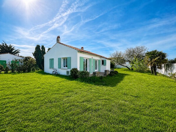 Une maison blanche avec des volets verts et un toit en tuiles, entourée d’une pelouse bien entretenue.
