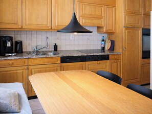 A kitchen with wooden cabinets, a granite countertop, a black pendant light, a coffee maker, and a dishwasher.