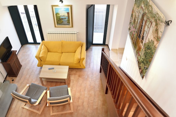 A living room with a yellow sofa, two armchairs, a coffee table, a TV, and a painting on the wall.