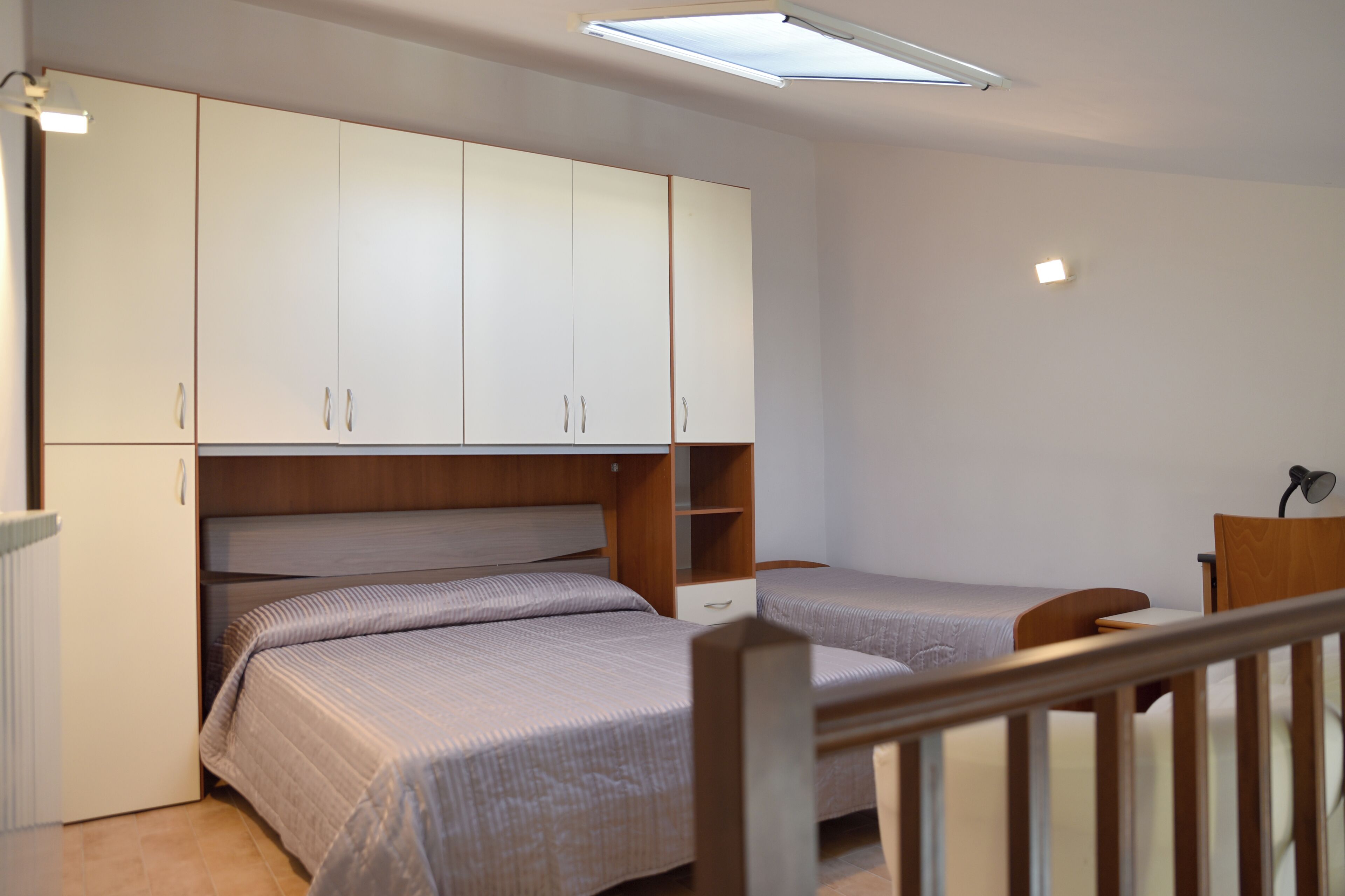 Een slaapkamer met twee enkele bedden, een houten bureau en een witte kast.