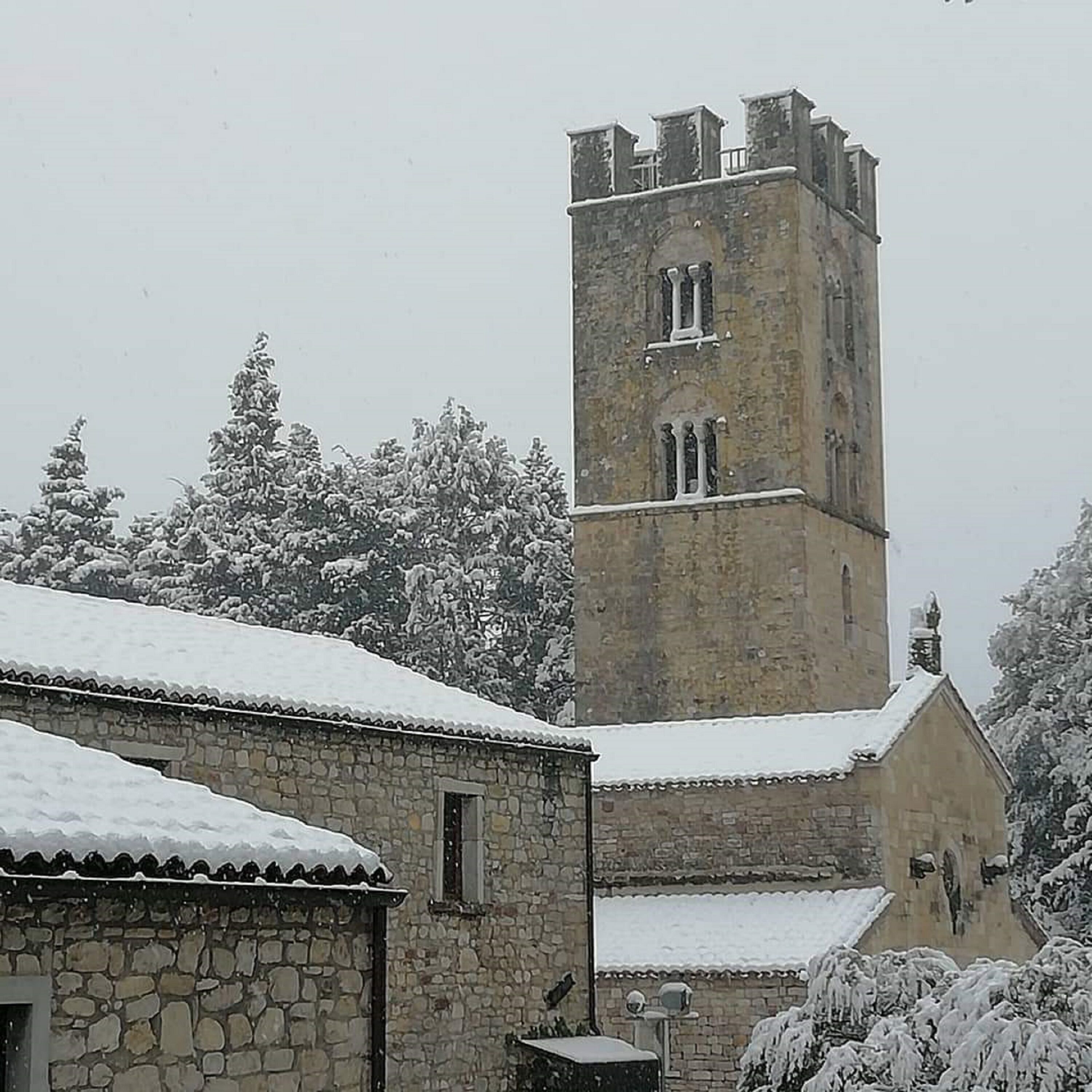A stone building with a tower, snow-covered trees, and a clear sky.