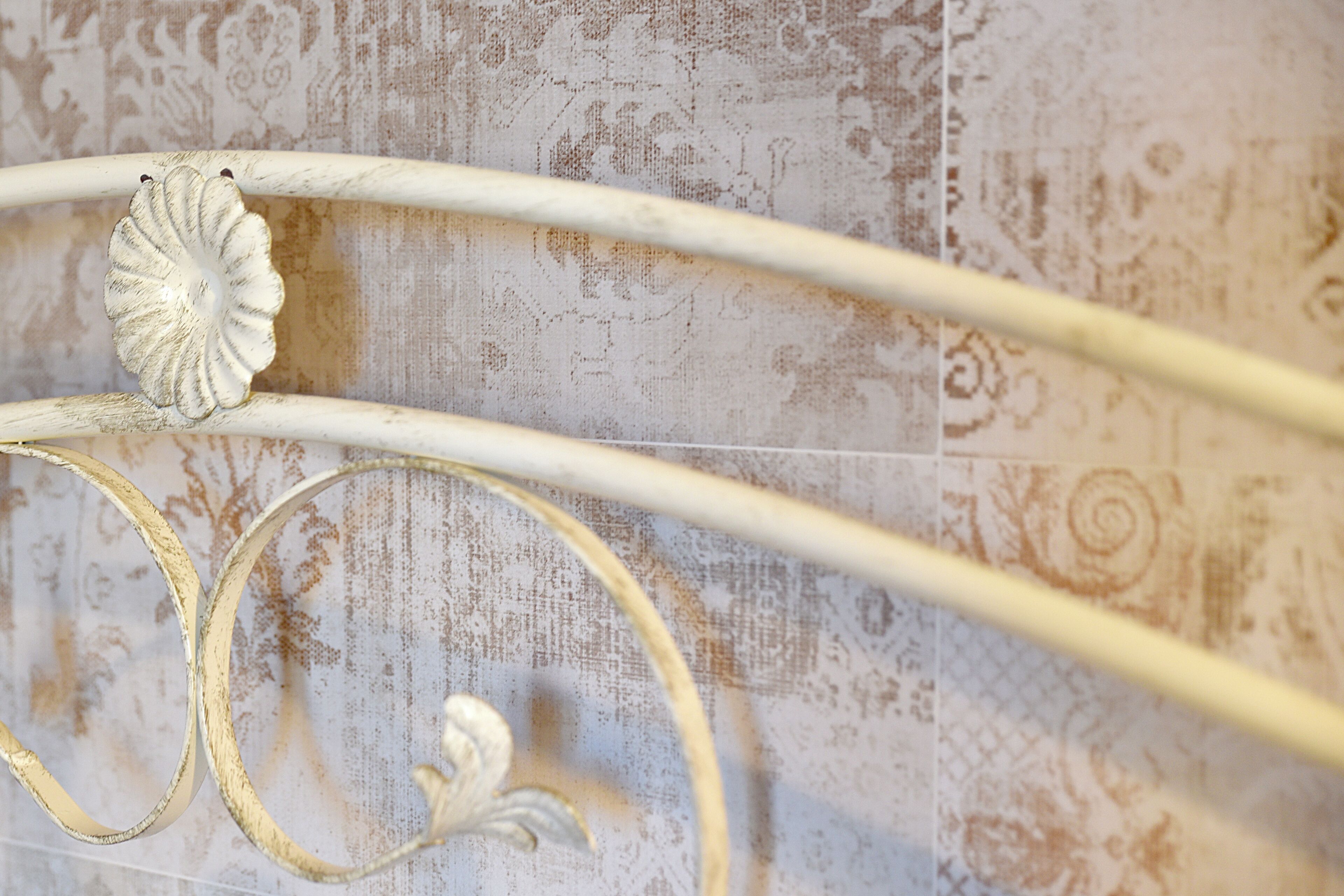 Estructura de cama metálica con diseños ornamentales y una pared texturizada de fondo.