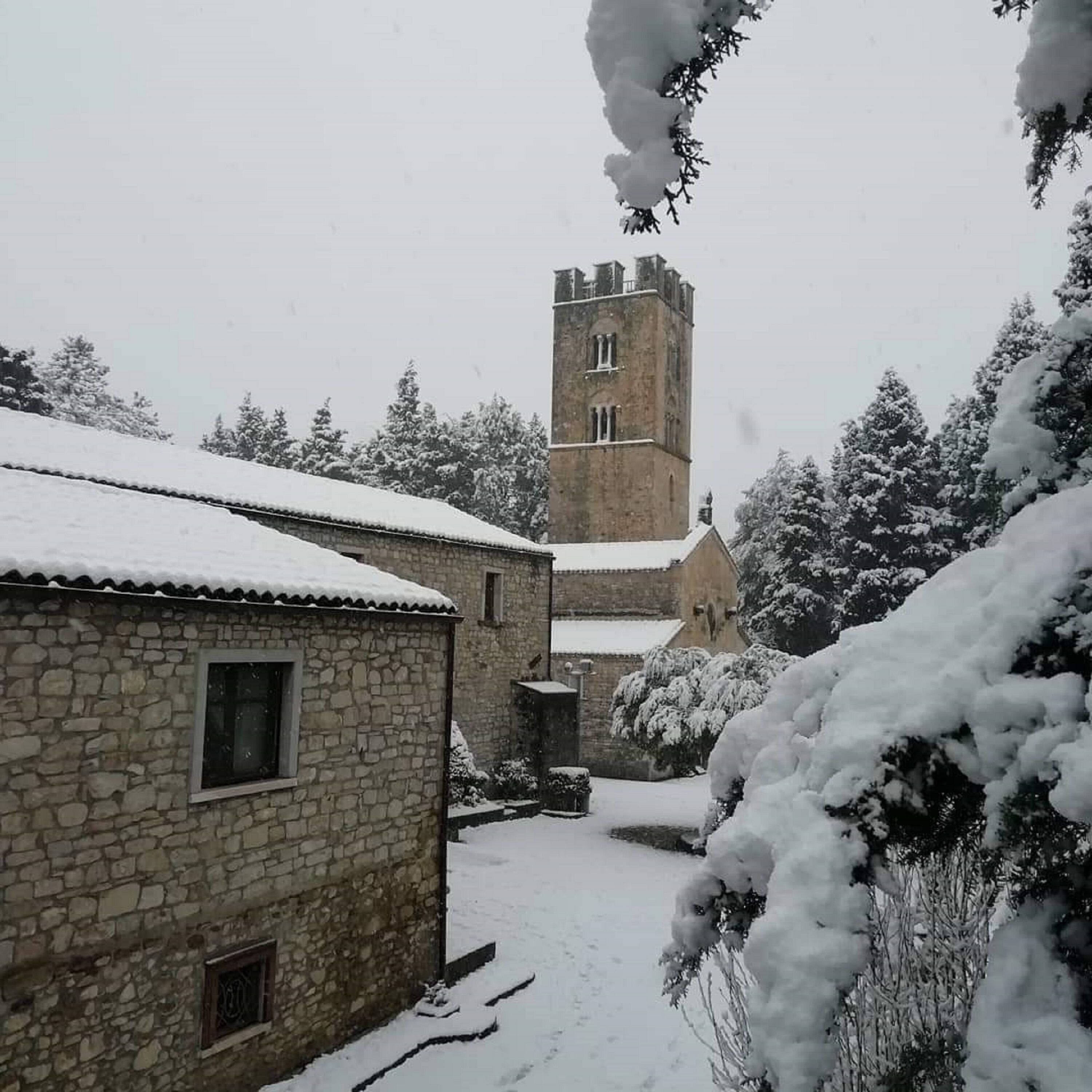 Un edificio de piedra con techo nevado, una torre con reloj y árboles cargados de nieve.