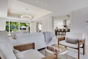 Un salon moderne avec un canapé, des fauteuils, une table basse sur laquelle sont disposés des jeux d’échecs, et une vue sur l’espace repas.