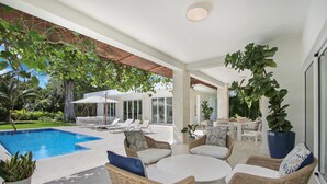 A modern outdoor lounge area with a pool, wicker furniture, and large windows. - Las Palmas 12: 4BR tranquil heaven near golf & beach w/ pool, golf cart, and staff (Punta Cana)