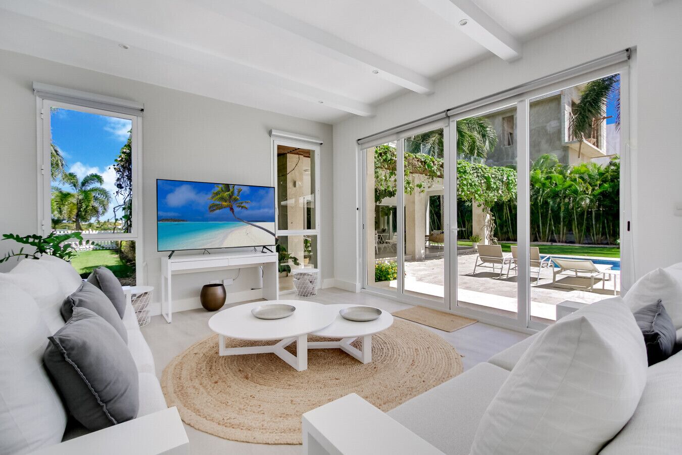 Ein modernes Wohnzimmer mit Flachbildfernseher, einer Couch, einem Couchtisch und Blick auf Pool und Garten durch große Schiebeglastüren.