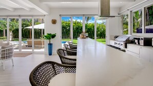 A modern kitchen with a large island, outdoor seating, and a view of a pool and greenery. - Las Palmas 12: 4BR tranquil heaven near golf & beach w/ pool, golf cart, and staff (Punta Cana)